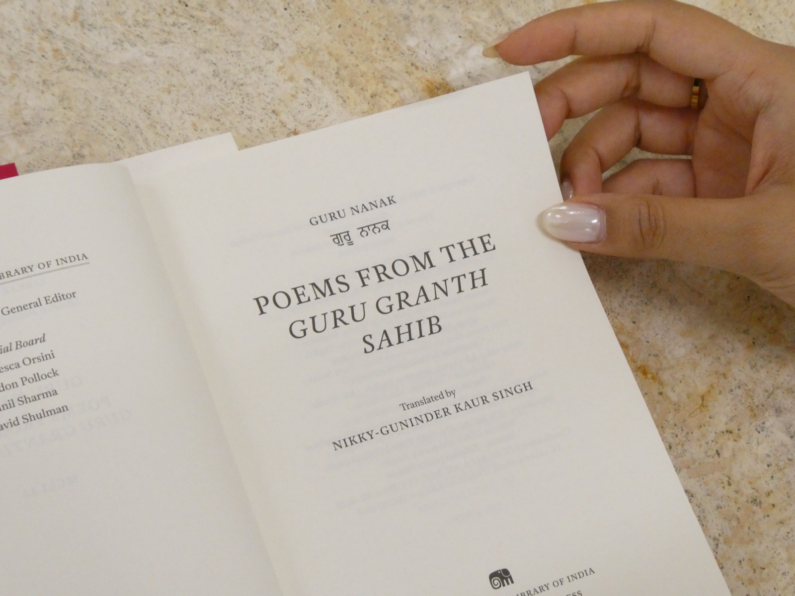 A hand on the title page of Poems from the Guru Granth Sahib, showing ਗੁਰੂ ਨਾਨਕ in Gurmukhi